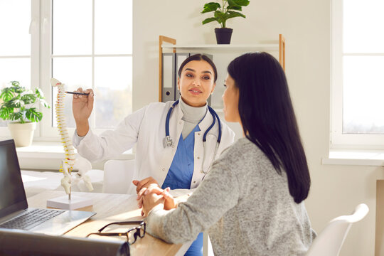 Portrait of female doctor physiotherapist or orthopedist showing to her woman patient model of spine in her office giving consultation about scoliosis or spinal problems during medical exam.