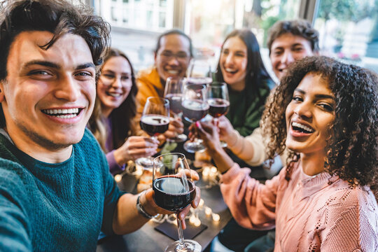 Multiracial friends drinking and toasting red wine at bar table- Group of happy young people taking selfie picture at restaurant-Life style concept with youth guys enjoying happy hours 