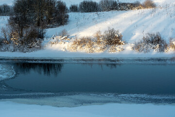 Winter landscape with a frozen river and icy shores on a sunny winter day.