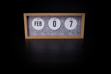 A wooden calendar block showing the date February 7th on a dark black background, save the date or date of event concept