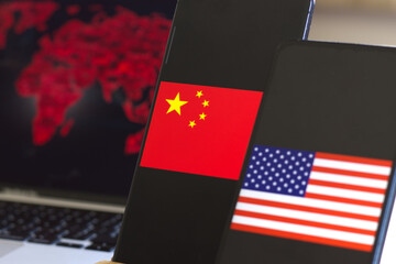 American and China flags on the smartphone screen. World map in the background on computer screen. 