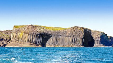 Tourists walking on the famous island of Staffa, consisting of dark hexagonal basalt columns, Inner...