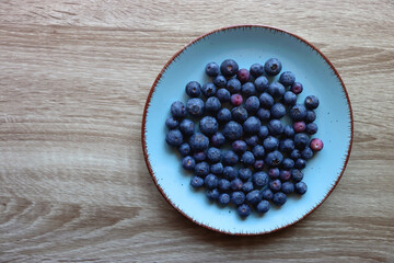 Turquoise plate with fresh blueberries on wooden background. Top view.