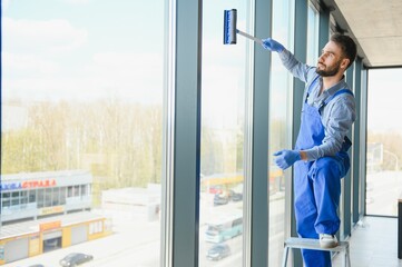 Male professional cleaning service worker in overalls cleans the windows and shop windows of a store with special equipment