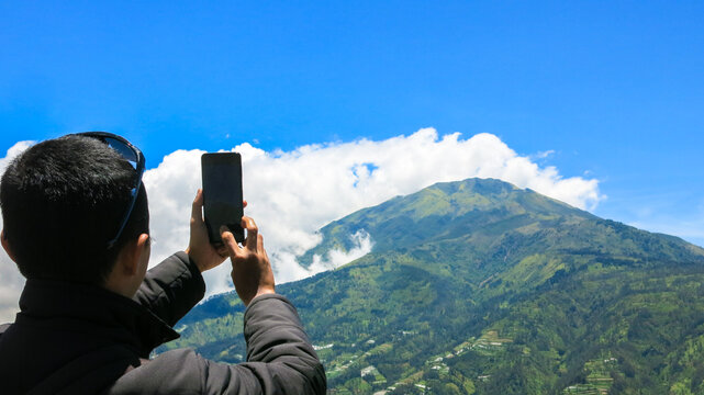 a young traveller man taking portrait picture of beautiful mountain and sky scenery view using his smartphone. healthy lifestyle outdoor activity.