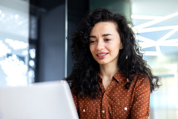 Happy and smiling hispanic businesswoman typing on laptop, office worker with curly hair and...