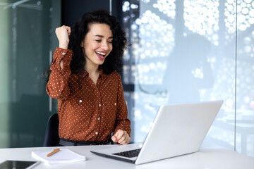 Hispanic business woman celebrating victory success, employee with curly hair inside office reading...