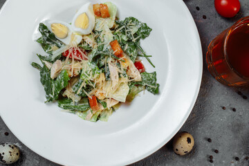 Traditional caesar salad in a white bowl on a old white table with leaves and a sauce boat and parmesan. Selected focus.