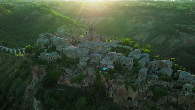 Aerial footage of the hilltop Civita di Bagnoregio Village with a linking bridge in Italy. Close-up view from above of a golden sunset over the medieval Italian town with stone houses in 4K ProRes.