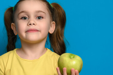 Fototapeta na wymiar A little girl is holding a green apple on a blue background.
