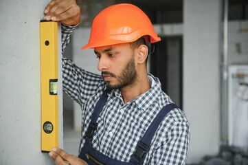 Indian construction site manager standing wearing helmet, thinking at construction site. Portrait of mixed race manual worker or architect.