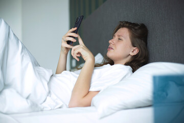 Girl with vision problems tries to read text on the phone. Bad vision concept. Woman looking at the screen of a mobile phone, having vision problems. selective focus in bed in bedroom in the morning 