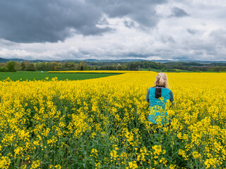 A woman in a blue jacket stands in cloudy rainy weather in the middle of an oilseed rape field in the enclave of Busingen, Germany.
