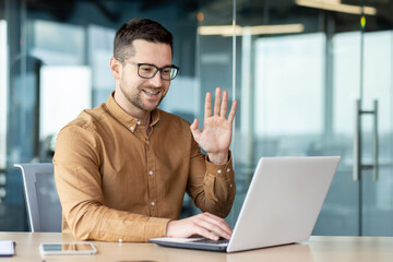 A young businessman works in the office at a laptop and communicates on a video call. Online...