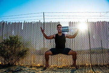 Man in yoga pose with intense pranayama or  breath work sticking his tongue out to cleanse his system in front of a boundary fence with Beware Of Dog sign. 