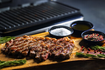 ribeye steak on wooden board with spices and electric grill