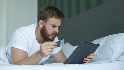 Nervous sad upset confused young man, stressed worried guy having problem with paying, buying online, payments with credit blocked bank card, looking at screen, monitor of laptop. Internet fraud