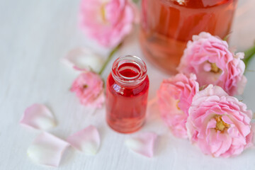 Composition with pure natural organic rose essential oil in glass bottle, luxury perfumery ingredient for premium fragrance, skin care products, anti-age beauty treatment. Fresh flowers