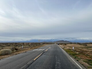 Desert highway, leading straight to foothills and mountains in Southern California on an overcast day. Car stopped at side of the road