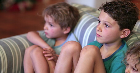 Siblings watching TV screen in night-time on sofa