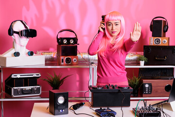 Asian musical artist standing at dj table doing stop gesture with palm, having hegative expression,...