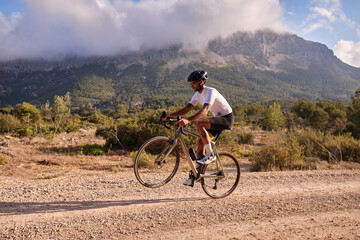 Man cyclist on gravel bicycle riding wheelie on a rear wheel.Cyclist practicing on gravel road.Gravel biking. Extreme sports and activity concept.Spain - obrazy, fototapety, plakaty