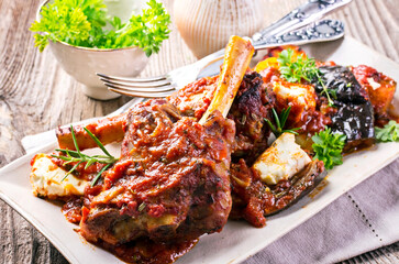 Traditional Greek braised lamb knuckle with feta cheese and eggplant in spicy tomato sauce served...