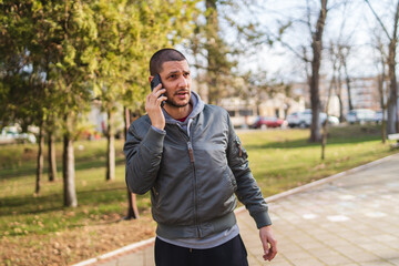 A man using and talking on his phone outside in park during the day