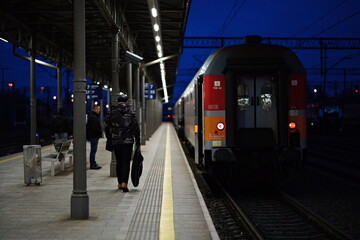 Ludzie czekający na peronie dworca kolejowego przy pociągu na tle nocnego nieba