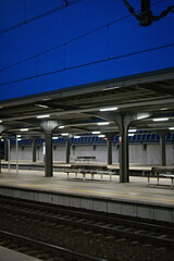 Pusty peron na dworcu kolejowym oświetlony lampami na tle nocnego nieba - obrazy, fototapety, plakaty