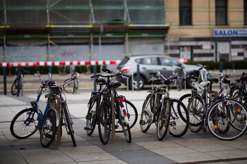 Parking dla rowerów przy miejskiej ulicy z wieloma rowerami przypiętymi do niego, w tle budowa i samochody na ulicy - obrazy, fototapety, plakaty