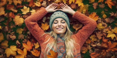 Young beautiful woman with long blonde hair and knitted hat lying down on autumn leaves
