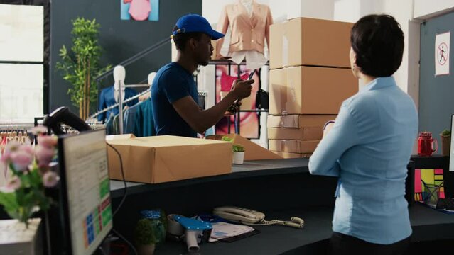 African american courier taking photo of carton boxes using tablet computer before putting store manager to sign delivery report. Employee preparing packages for shipping in modern boutique