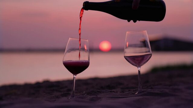Filling wineglasses with red champagne on sea sand beach