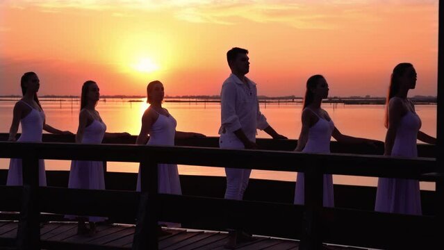 Ballet dancers in suits standing on old bridge at sunset
