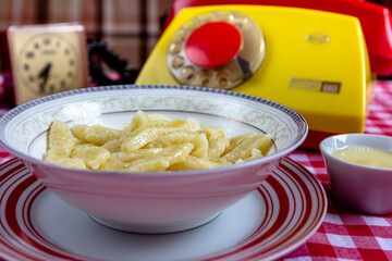 Russian and Ukrainian cuisine. Lazy dumplings with sugar, butter and sour cream in a white plate with a spoon on a light grey background. Flatlay, top view. Background image, copy space