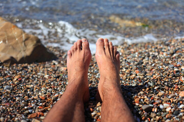 Man Feet Relax on The beach Pebbles. Relaxation and summertime concept. The young male setting...
