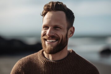 Portrait of handsome man smiling while standing on beach during autumn day