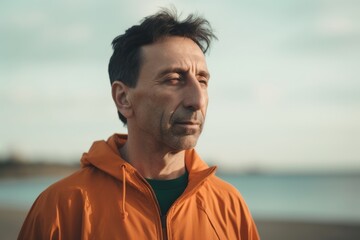 Fototapeta premium Mature man in orange jacket standing on the beach and looking away