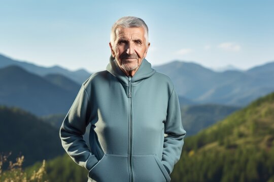 Senior Man In Sportswear Standing On Top Of Mountain And Looking At Camera