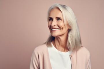 Portrait of a beautiful senior woman smiling at the camera while standing against pink background
