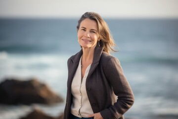 Fototapeta na wymiar Portrait of smiling businesswoman standing with hands in pockets on the beach