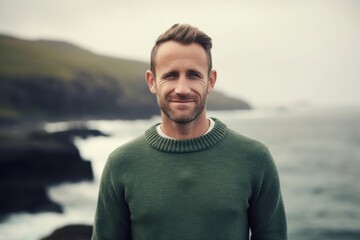 Portrait of a handsome man in a green sweater standing by the ocean