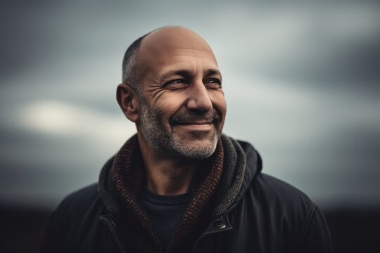 Portrait of a bald man in a black jacket on a cloudy day.