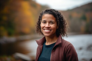 Portrait of a smiling young woman standing by the river in autumn