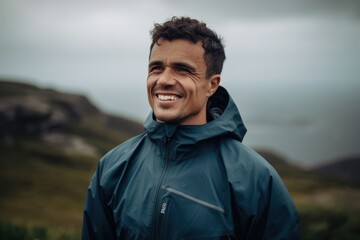 Handsome young man in a blue jacket standing on the top of a mountain and laughing