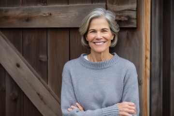 Portrait of smiling senior woman standing with arms crossed against wooden wall