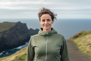 Fototapeta premium Portrait of smiling mature woman standing at edge of cliff with ocean in background