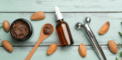 Bottle of almond essential oil, natural scrub and massage tool on wooden background