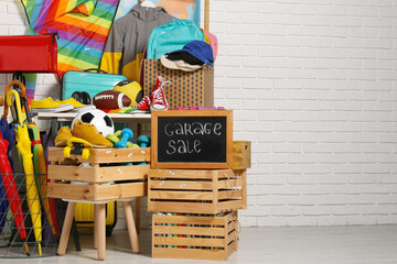 Sign Garage Sale written on blackboard near many different stuff indoors. Space for text